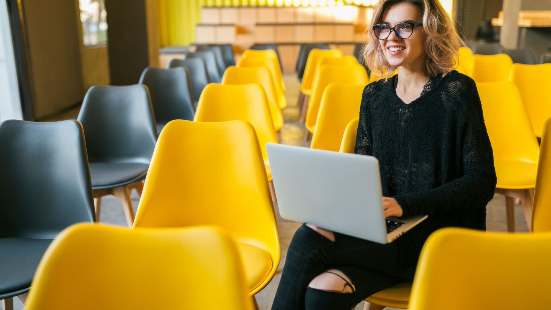 portrait of young woman sitting in lecture hall, working on laptop